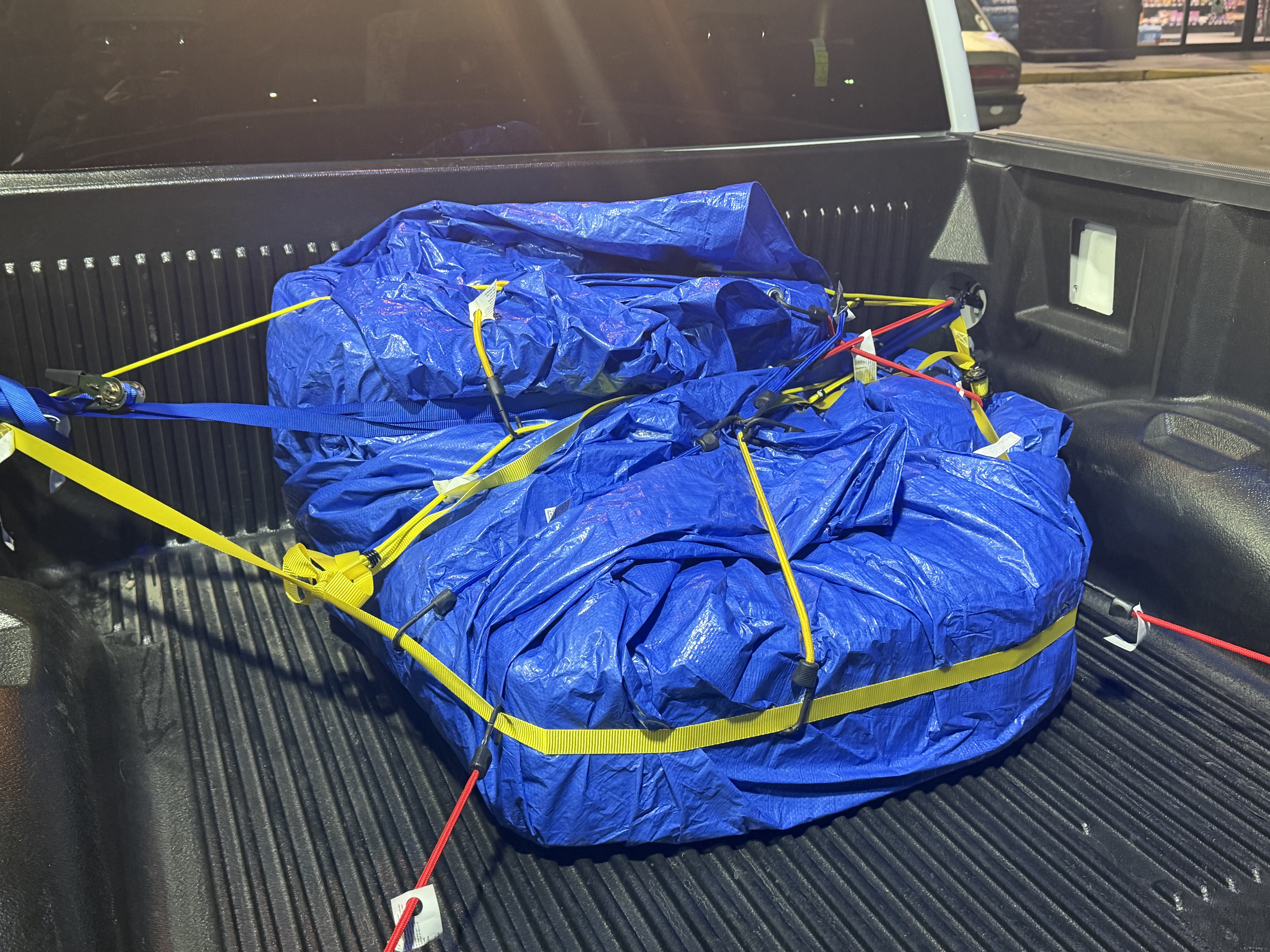 A blue-tarped pile of batteries strapped down in the bed of the F-150 with yellow ratchet straps and red bungees.