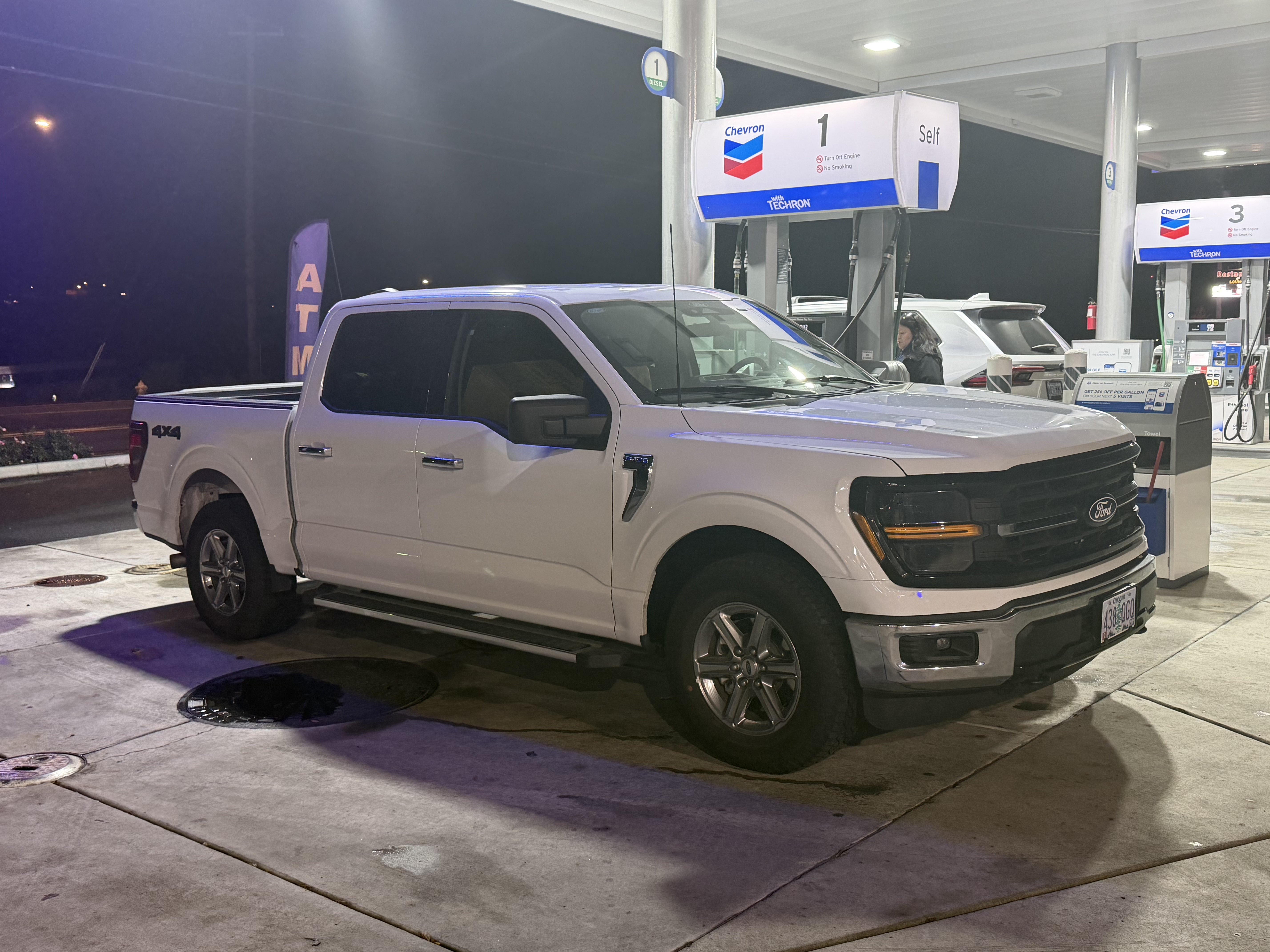 The white F-150 parked under the awning of a Chevron station at night, mid-drive home from Idaho.