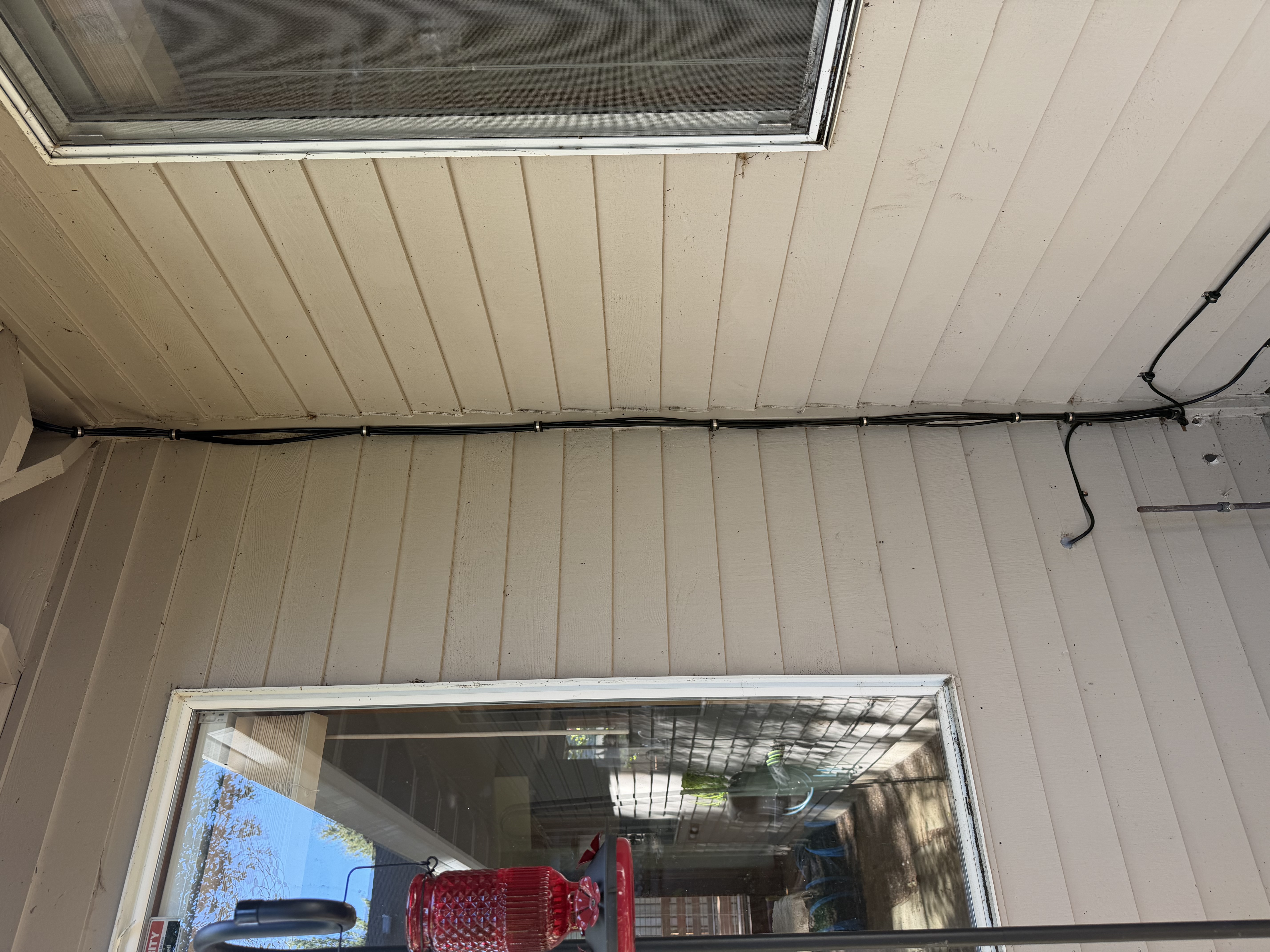 A bundle of black cables running down the exterior corner of the house, clipped to the siding at regular intervals between two windows.