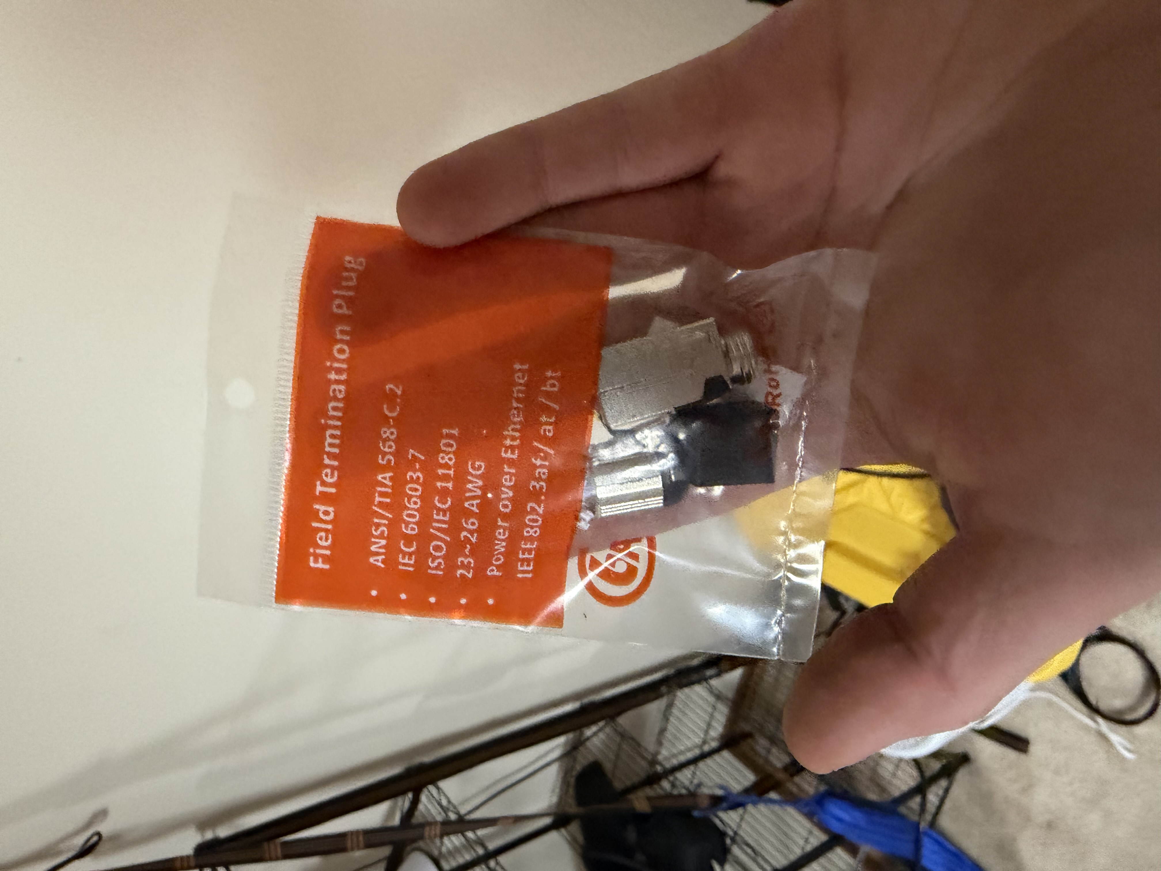 A hand holding a clear plastic bag of TP-Link field termination plugs, with an orange label listing specs: ANSI/TIA 568-C.2, 23–26 AWG, Power over Ethernet IEEE 802.3af/at/bt.